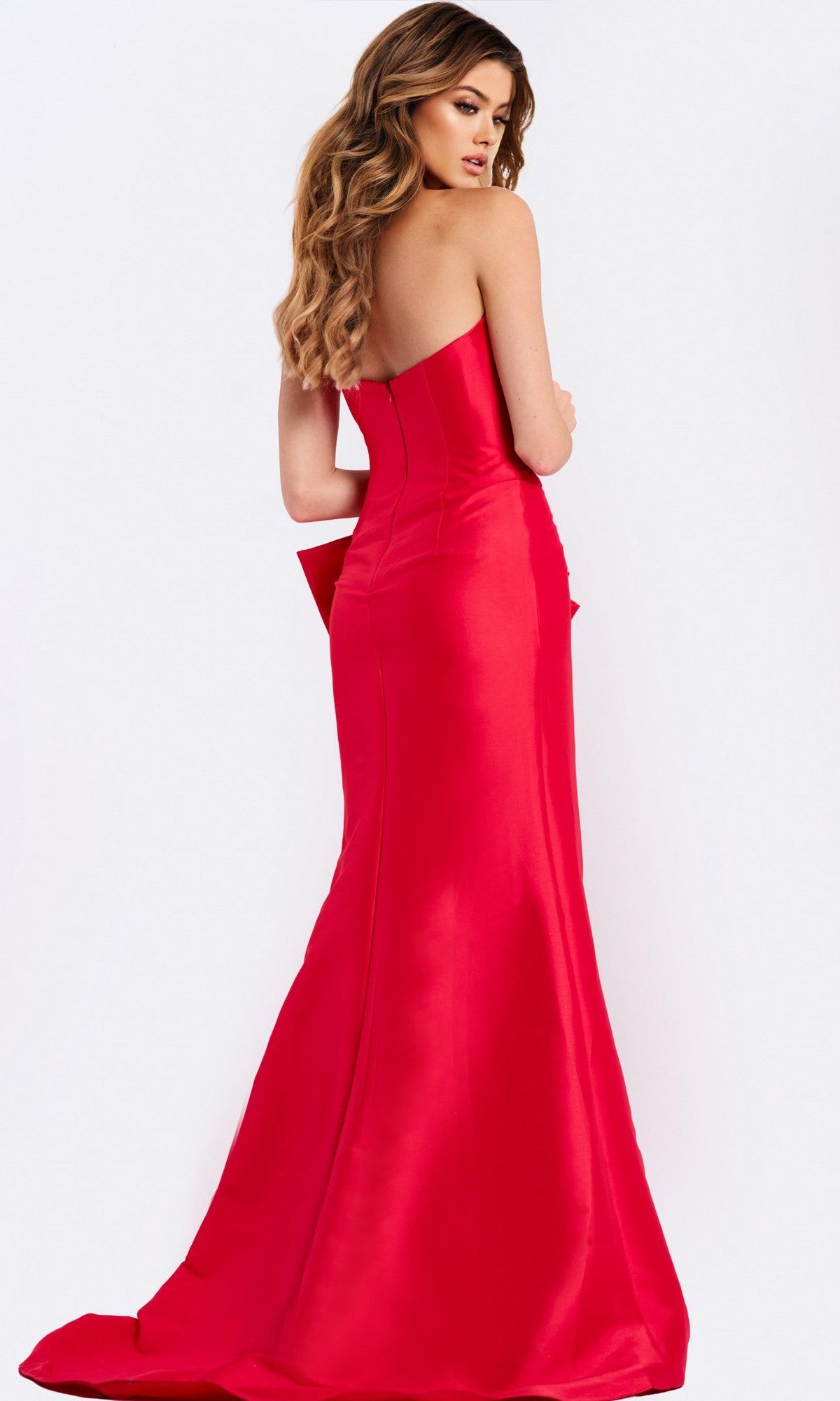 A woman with long wavy hair models the Jovani 49195, a form-fitting, strapless satin prom dress with a slight train, posing with her back to the camera against a plain white background.